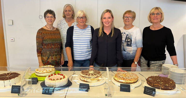 Frisch gebackene Kuchen im Café Jahreszeit: Sechs Frauen stehen hinter einem Tisch mit verschiedenen Kuchen und Torten.