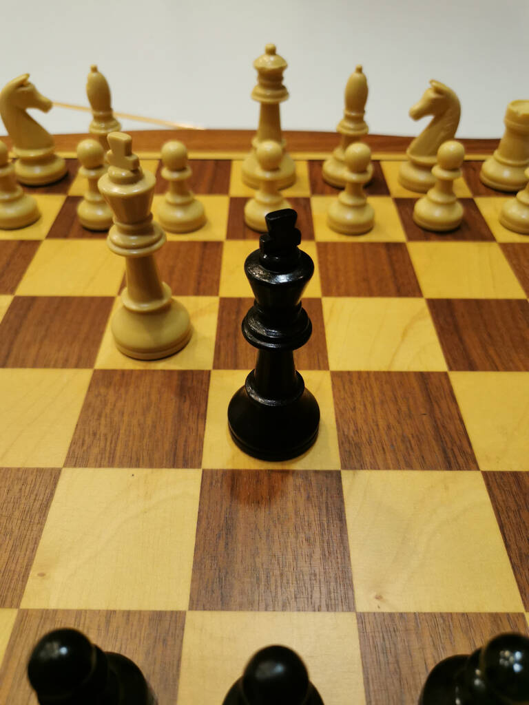 Schach-Treff: Auf einem Schachbrett steht ein schwarzer König umgeben von weißen Figuren.