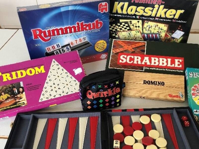 Spieletreff im Bürgertreff iAuf dem Bild sind verschiedene Gesellschaftsspiele wie Rummikub, Scrabble, Tridom, Quirkle, Domino und Skyo zu sehen, die auf einem Tisch ausgebreitet sind.